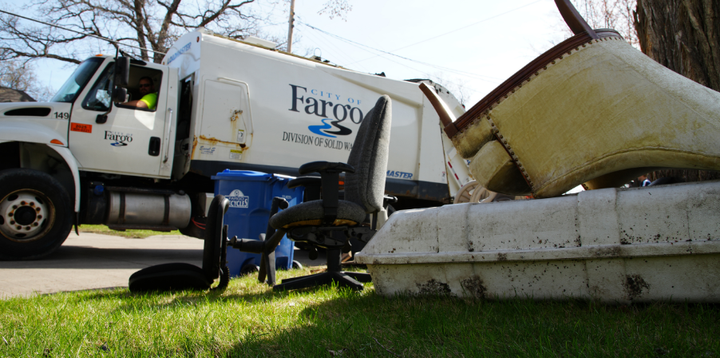 Household junk sits on a boulevard with a City of Fargo garbage truck in the street nearby.