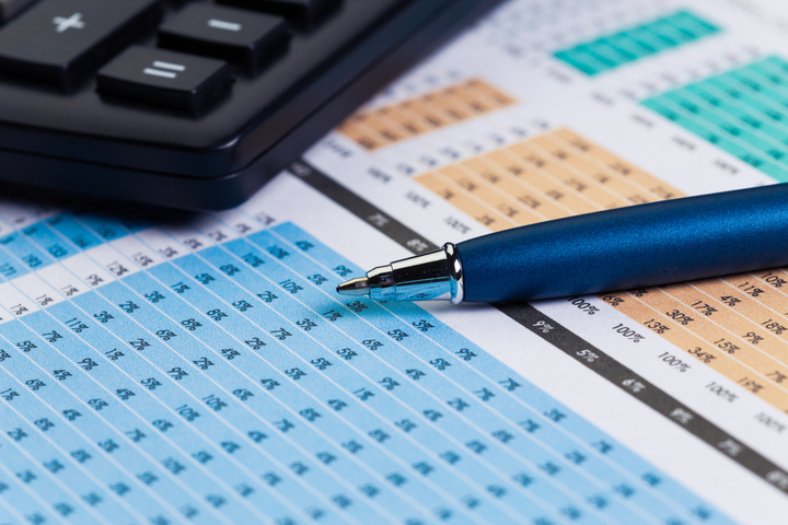 A pen and calculator rest on a spreadsheet with numbers.