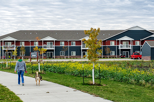 A person walks a dog on a sidewalk by an apartment building