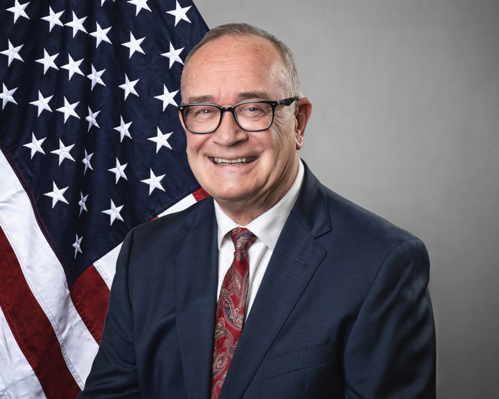 Deputy Mayor John Strand appears in front of an American flag.